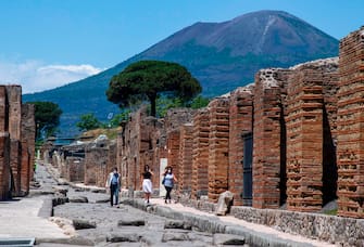 Visitors walk across the archeological site of Pompeii at the bottom of the Mount Vesuvius volcano (Rear) on May 26, 2020, as the country eases its lockdown aimed at curbing the spread of the COVID-19 infection, caused by the novel coronavirus. - Italy's world-famous archeological site Pompeii reopened to the public on May 26,bBut with foreign tourists still prohibited from travel to Italy until June, the site that attracted just under 4 million visitors in 2019 is hoping that for now, Italian tourists can make up at least a fraction of the difference. (Photo by Tiziana FABI / AFP) (Photo by TIZIANA FABI/AFP via Getty Images)