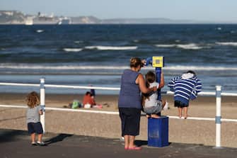 1227636632 WEYMOUTH, DORSET - MAY 28: Members of the public look through a view finder at the beach front on May 28, 2020 in Weymouth, Dorset. The British government continues to ease the coronavirus lockdown by announcing schools will open to reception year pupils plus years one and six from June 1st. Open-air markets and car showrooms can also open from the same date. (Photo by Naomi Baker/Getty Images)