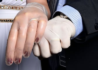 TOPSHOT - Newly-wed Italians Ester Concilio (L) and Rafaele Carbonelli show wedding rings under the protective gloves following the ceremony at the Briosco's town hall, about 45 km ( 28 miles) north of Milan, on May 11, 2020 during the country's lockdown aimed at curbing the spread of the COVID-19 infection, caused by the novel coronavirus. (Photo by Miguel MEDINA / AFP) (Photo by MIGUEL MEDINA/AFP via Getty Images)