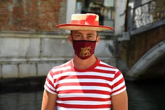 A gondolier, wearing a face mask showing the winged lion of Venice, looks on prior to going for a gondola ride with customers on a canal in Venice on June 12, 2020 as the country eases its lockdown aimed at curbing the spread of the COVID-19 infection, caused by the novel coronavirus. (Photo by ANDREA PATTARO / AFP) (Photo by ANDREA PATTARO/AFP via Getty Images)