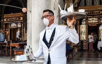 TOPSHOT - A waiter serves customers on June 12, 2020 at the terrace of the 18th Century Cafe Florian on St. Mark's Square in Venice, which reopens after being closed for three months during the country's lockdown aimed at curbing the spread of the COVID-19 infection, caused by the novel coronavirus. (Photo by ANDREA PATTARO / AFP) (Photo by ANDREA PATTARO/AFP via Getty Images)