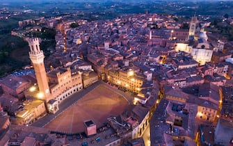 View on the main square "Il Campo" and the "il Mangia" tower upon the Council palace, left, and the Cathedral, right, of the medieval town of Siena on twilight during the lockdown emergency period aimed at stopping the spread of the Covid-19 coronavirus. Although the lockdown and full absence of people, the scenery of the Italian squares and monuments remain fascinating, Siena, Italy, 23 April 2020(ANSA foto Fabio Muzzi)