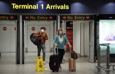 Passenger swearing PPE (personal protective equipment), including a face mask as a precautionary measure against COVID-19, push their suitcases after arriving at Terminal 1 of Manchester Airport in northern England, on June 8, 2020, as the UK government's planned 14-day quarantine for international arrivals to limit the spread of the novel coronavirus begins. (Photo by Oli SCARFF / AFP) (Photo by OLI SCARFF/AFP via Getty Images)