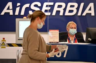 An airport personnel wearing a protective face mask, serves a passenger behind plexiglas at the check-in counter at Belgrade's airport on May 21, 2020, as Serbia's national carrier, Air Serbia, resumes commercial flights following the government's easing of lockdown measures against the spread of the novel coronavirus, COVID-19, pandemic. - With limited number of flights, air travel has resumed at Serbia's main airport after the authorities approved the airport to gradually resume operations with new guidelines amid the COVID-19 pandemic. Only passengers with tickets are allowed into the airport building four hours ahead of their flight. (Photo by Andrej ISAKOVIC / AFP) (Photo by ANDREJ ISAKOVIC/AFP via Getty Images)