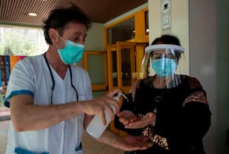 A woman wearing a face mask and shield is helped sanitize her hands as she arrives on May 6, 2020 at the Tor Vergata Covid hospital in Rome, during the country's lockdown aimed at curbing the spread of the COVID-19 infection, caused by the novel coronavirus. (Photo by Tiziana FABI / AFP) (Photo by TIZIANA FABI/AFP via Getty Images)