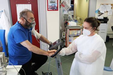 GENOA, ITALY - JULY 24: Recovered Coronavirus patient Remo Giacometti, 72-years-old, is comforted by a medical staff as he uses an exercise bike at the Department of Rehabilitative Cardiology of ASL 3 Genova on July 24, 2020 in Genoa, Italy. Remo, who has been an underwater diver for many years, suffers from respiratory diseases that force him to use an oxygen cylinder to breathe. Because of Covid-19 he remained in hospital for three months. There is an estimated 14 million confirmed Coronavirus cases worldwide, with a reported 8 million recovering patients. In 80 percent of COVID-19 cases, recovery is complicated, leaving physical and psychological consequences that do not easily subside or allow survivors to return to normal life. The first Covid veterans gym, a project of Genoa's ASL 3 and rehabilitation cardiology department directed by cardiologist Piero Clavario, aims to address this. Designed to reactivate the heart, muscles and lungs, the gyms rehabilitation process gives patients a 2-month protocol, overseen by a staff of four doctors, three nurses, one psychologist and a physiotherapist. Of approximately 700 patients who were previously hospitalized with Covid, 100 patients were selected to participate in the gym, with the first 12 patients now six weeks into their rehabilitation process. Treatment is designed to combat numerous effects of the disease. Half of all patients hospitalized for Covid will be left with lung fibrosis, causing difficulty breathing. The nervous system is also affected as evidenced by the loss of taste and smell. Meanwhile 80 percent of patients suffer cognitive impairments such as memory loss and orientation difficulties, 40 percent show symptoms of depression and others experience chronic fatigue and rapid weight loss. (Photo by Marco Di Lauro/Getty Images)