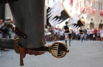 SIENA, ITALY - AUGUST 16: Members of the Contrada della Lupa walk the streets during a procession before the annual Palio dell'Assunta horse-race on August 16, 2013 in Siena, Italy.The so-called Duce holds a word, while flag-swingers act in the background. The Palio races in Siena, in which riders representing city districts compete,and takes place twice a year in the summer in a tradition that dates back to 1656.