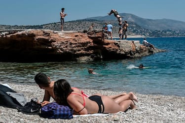 Sunbathers watch a young man doing a backflip into the water as they lie on the beach in Athen's southern suburb on May 9, 2020, as the nations readies for the reopening of schools and most of shops starting May 11. (Photo by Louisa GOULIAMAKI / AFP) (Photo by LOUISA GOULIAMAKI/AFP via Getty Images)