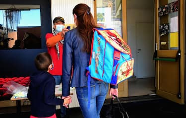 BORGOSESIA, ITALY - MAY 12:  A school worker measures the temperature of a woman and her son before attending lessons in a classroom with school desks spaced apart to respect social distancing measures to counter the spread of COVID-19 on May 12, 2020 in Borgosesia, Italy. Italy was the first country to impose a nationwide lockdown to stem the transmission of the Coronavirus (Covid-19), but this project by the Borgosesia maYor aims to open schools with the correct safety measures.  (Photo by Pier Marco Tacca/Getty Images)