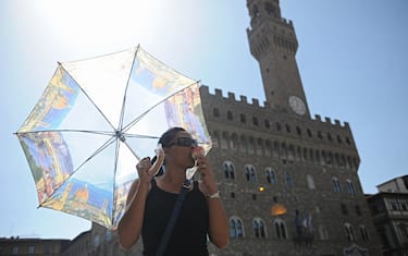 Una donna mangia un gelato e si protegge con un ombrello dal sole a Firenze, 21 giugno 2012.
ANSA/MAURIZIO DEGL' INNOCENTI