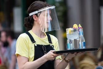 CARDIFF, WALES - AUGUST 12: A woman wearing a plastic face visor serves drinks outdoors at Gin and Juice gin bar on August 12, 2020 in Cardiff, Wales. Coronavirus lockdown measures continue to be eased as the number of excess deaths in Wales falls below the five-year average. (Photo by Matthew Horwood/Getty Images)