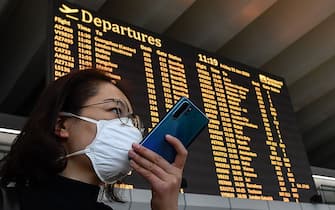 A passenger wearing a respiratory mask speaks on her smartphone by the departures board on January 31, 2020 at Rome's Fiumicino airport, as a number of airlines halted or reduced flights to China as the country struggles to contain the spread of the deadly novel coronavirus. - The Italian government said on January 30, 2020 it was suspending all flights between Italy and China, adding it was the first EU government to do so. China has advised its citizens to postpone trips abroad and cancelled overseas group tours, while several countries have urged their citizens to avoid travel to China. (Photo by Tiziana FABI / AFP) (Photo by TIZIANA FABI/AFP via Getty Images)