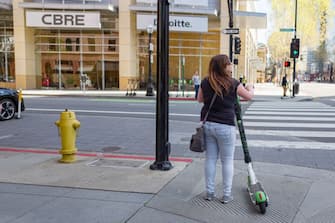 View from behind of woman holding a Lime micromobility scooter and preparing to cross intersection in the Silicon Valley town of San Jose, California, April 13, 2019. (Photo by Smith Collection/Gado/Getty Images)