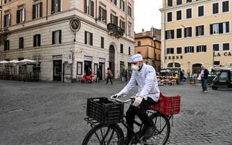 A cook wearing a respiratory mask as part of precautionary measures against the spread of the new COVID-19 coronavirus, rides a bicycle across a deserted Campo Dei Fiori square in downtown Rome on March 10, 2020 as Italy imposed unprecedented national restrictions on its 60 million people on March 10 to control the deadly coronavirus. (Photo by Alberto PIZZOLI / AFP) (Photo by ALBERTO PIZZOLI/AFP via Getty Images)