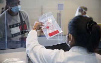 CASELLE TORINESE, ITALY - AUGUST 26: A female medical staff hands a Covid 19 control swab test kit to a traveler on August 26, 2020 in Turin, Italy. At Italian airports, all travelers from countries at risk of Covid-19 are tested with swabs to prevent the spread of Covid 19 in Italy. (Photo by Stefano Guidi/Getty Images)