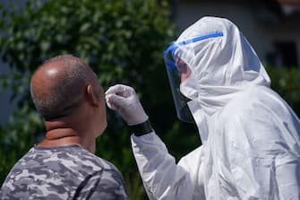 GUETERSLOH, GERMANY - JUNE 23: A soldier of the Bundeswehr dressed in full PPE takes a throat swab sample from a local resident in the town of Rheda following a Covid-19 outbreak at the nearby Toennies meat packaging plant during the coronavirus pandemic on June 23, 2020 near Guetersloh, Germany. State authorities announced today they are placing the entire Guetersloh region into lockdown following confirmed Covid-19 infection in over 1,500 employees of the plant. The Bundeswehr, the German armed forces, has stepped in to help test people at the approximately 250 houses and apartment complexes where Toennies employees, many of whom come from Romania, Bulgaria and Poland, live throughout the Guetersloh region. (Photo by Sean Gallup/Getty Images)