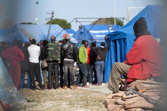 Un capannello di braccianti intorno alla tenda incendiata dove è morto un migrante la notte scorsa in un incendio divampato nella nuova tendopoli gestita prima dal Comune ed ora dalla Caritas a San Ferdinando, 22 marzo 2019. 
ANSA/Marco Costantino