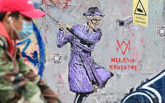 A man wearing a protective mask passes by a new mural by Italian street artist TvBoy, entitled "Milano resist" on October 27, 2020 in Naviglio neighbourhood, southern Milan. (Photo by MIGUEL MEDINA / AFP) / RESTRICTED TO EDITORIAL USE - MANDATORY MENTION OF THE ARTIST UPON PUBLICATION - TO ILLUSTRATE THE EVENT AS SPECIFIED IN THE CAPTION (Photo by MIGUEL MEDINA/AFP via Getty Images)