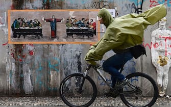 A man rides his bike in front of a new mural by Italian street artist TvBoy, entitled "Supper for six", inspired by "The last supper" by Italian artist Leonardo da Vinci on October 27, 2020 in Naviglio neighbourhood, southern Milan. (Photo by MIGUEL MEDINA / AFP) / RESTRICTED TO EDITORIAL USE - MANDATORY MENTION OF THE ARTIST UPON PUBLICATION - TO ILLUSTRATE THE EVENT AS SPECIFIED IN THE CAPTION (Photo by MIGUEL MEDINA/AFP via Getty Images)
