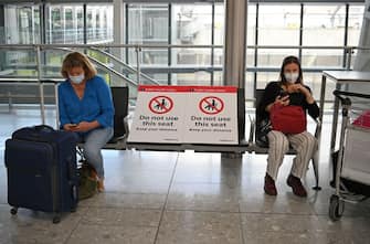 Passengers wearing face masks or covering due to the COVID-19 pandemic, sit socially distanced with their luggage at Heathrow airport, west London, on July 10, 2020. - The British government on Friday revealed the first exemptions from its coronavirus quarantine, with arrivals from Germany, France, Spain and Italy no longer required to self-isolate from July 10. Since June 8, it has required all overseas arrivals -- including UK residents -- to self-quarantine to avoid the risk of importing new cases from abroad. (Photo by DANIEL LEAL-OLIVAS / AFP) (Photo by DANIEL LEAL-OLIVAS/AFP via Getty Images)
