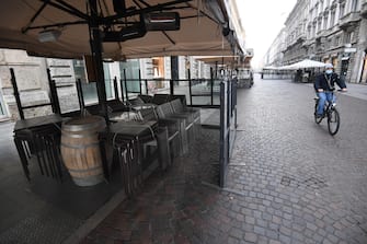 A man with his face covered by a medical mask passes by bicycle next to the tables and stacked chairs of the outdoor area of a bar in the central pedestrian street of Via Dante closed in compliance with anti-covid measures in the Brera district, Milan, Italy 16 November 2020. ANSA/DANIEL DAL ZENNARO&nbsp;