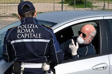 A member of the Rome Local Police checks the documents and the self-declaration of a motorist, wearing a facemask for protective reasons, on the Via Pontina, in Rome, on March 21, 2020, during the country's lockdown aimed at stopping the spread of the COVID-19, the novel coronavirus. - Italy reported a record 627 new coronavirus deaths on March 20, 2020 and saw its world-topping toll surpass 4,000, despite government efforts to stem the pandemic's spread. (Photo by Alberto PIZZOLI / AFP) (Photo by ALBERTO PIZZOLI/AFP via Getty Images)