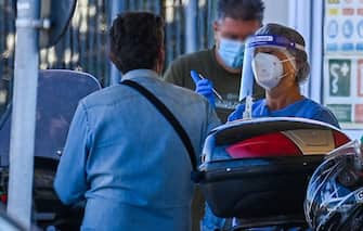 A holidaymaker on a motorbike (L) returning from Sardinia by ferry undergoes a compulsory drive-through swab test on August 23, 2020 at the port of Civitavecchia, northwest of Rome, during the COVID-19 infection, caused by the novel coronavirus. - Italy has recorded 1,071 new cases of coronavirus in the last 24 hours, breaking the symbolic barrier of 1,000 cases per day for the first time since May 12, according to an official report published on August 22, 2020. "61% (of these new cases) are linked to holiday returns," and more specifically 45% (97 cases) concern returns from the island of Sardinia, which had been spared by the first wave of the virus but where the comings and goings of careless tourists and revellers have contributed to the spread of the virus. (Photo by Vincenzo PINTO / AFP) (Photo by VINCENZO PINTO/AFP via Getty Images)