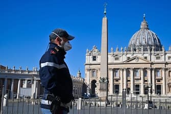 A police officer wearing a protective mask stands guard at the Vatican's Saint Peter's Square and its main basilica on March 11, 2020 a day after they were closed to tourists as part of a broader clampdown aimed at curbing the coronavirus outbreak. (Photo by ANDREAS SOLARO / AFP) (Photo by ANDREAS SOLARO/AFP via Getty Images)