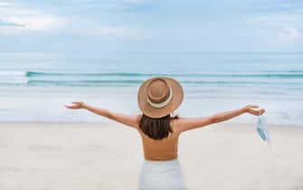 Beautiful young Asian traveler woman take off protective face mask at the beach. New normal, health care, travel and holiday concept