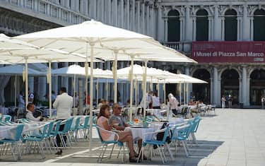 Turisti siedono ai tavoli sotto gli ombrelloni nel plateatico del caffè Aurora, in piazza San Marco, stamane 26 giugno 2020. ANSA/ANDREA MEROLA                               