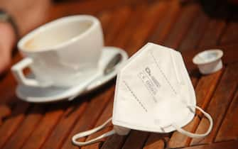 01 June 2021, Saxony-Anhalt, Quedlinburg: An FFP2 mask lies next to a cup of coffee on a table. In Saxony-Anhalt, outdoor and indoor catering has reopened under restrictions. Photo: Matthias Bein/dpa-Zentralbild/dpa (Photo by Matthias Bein/picture alliance via Getty Images)