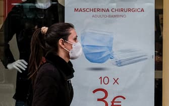 VOMERO DISTRICT, NAPLES, CAMPANIA, ITALY - 2021/01/11: A woman wearing protective mask passes in front of a shop window on the first day of sales where are an advertising poster promotes the offer of 10 surgical masks for 3 euros. (Photo by Antonio Balasco/KONTROLAB/LightRocket via Getty Images)