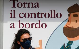 Una donna con la mascherina davanti a un manifesto che annuncia il ritorno dei controllori
