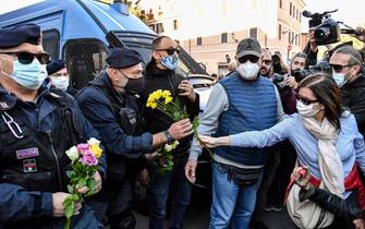 A woman hands flowers to police officers during a protest against the so-called Green Pass on October 15, 2021 at Circo Massimo in Rome, as new coronavirus restrictions for workers come into effect. - Italy braced for nationwide protests, blockades and potential disruption on October 15, 2021 as all workers must show a so-called Green Pass, offering proof of vaccination, recent recovery from Covid-19 or a negative test, or face being declared absent without pay. (Photo by Alberto PIZZOLI / AFP) (Photo by ALBERTO PIZZOLI/AFP via Getty Images)