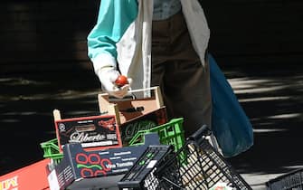 Una persona cerca cibo tra le cassette della frutta alla fine di un mercato rionale, a Milano