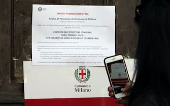 Una donna fotografa con il telefono cellulare i cartelli che comunicano l'obbligo del Green Pass per i dipendenti della sede degli Uffici del Comune di Milano
