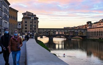 People walk at twilight along the Arno river near the Ponte Vecchio in downtown Florence, Tuscany, on November 14, 2020 during the COVID-19 pandemic caused by the novel coronavirus. - The Italian government imposed tighter restrictions on another five regions on November 10, including Tuscany, as it tries to stem escalating new cases of coronavirus, while still resisting a nationwide lockdown. (Photo by Vincenzo PINTO / AFP) (Photo by VINCENZO PINTO/AFP via Getty Images)