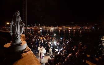 A priest (C) blesses the memorial for the shipwreck victims, as shipwreck survivors, relatives of victims, local residents and officials take part in a torchlight procession in the port of Giglio on January 13, 2022, marking the tenth anniversary of the January 13, 2012 Costa Concordia shipwreck off Giglio island, Tuscany, that killed 32. (Photo by Filippo MONTEFORTE / AFP) (Photo by FILIPPO MONTEFORTE/AFP via Getty Images)