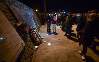 People stand by the memorial for the shipwreck victims, after shipwreck survivors, relatives of victims, local residents and officials took part in a torchlight procession in the port of Giglio on January 13, 2022, marking the tenth anniversary of the January 13, 2012 Costa Concordia shipwreck off Giglio island, Tuscany, that killed 32. (Photo by Filippo MONTEFORTE / AFP) (Photo by FILIPPO MONTEFORTE/AFP via Getty Images)