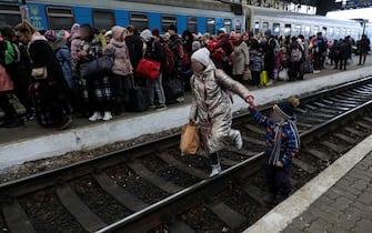 epa09806439 A woman walks with her child in a train line as displaced Ukrainians arrive at the Lviv train station in western Ukraine, to flee the Russian military operation, in Lviv, Ukraine, 05 March 2022 (issued on 06 March). Russian troops began a military operation in Ukraine on 24 February leading to a massive exodus of Ukrainians to neighboring countries as well as internal displacements.  EPA/MIGUEL A. LOPES