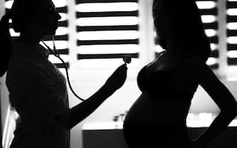 Silhouette female medicine doctor holding stethoscope to pregnant woman standing for encouragement, empathy, cheering, support, medical examination. New life of abortion concept. B / W style