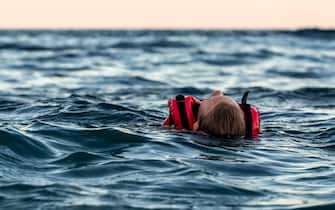 An unconscious drowning girl in a life jacket swims in a cold sea with waves at dusk. The danger of hypothermia. Rescue people on the waters. Man overboard on the high seas