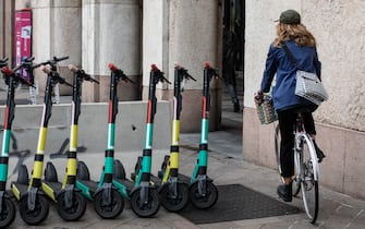 MILAN, ITALY - SEPTEMBER 23: A woman rides her bicycle past a series of electric scooters of the Dutch scooter rental company DOTT on Piazza San Babila on September 23, 2020 in Milan, Italy. Since the end of lockdown Milan authorities have added a further 35 kilometers of pop-up bike lanes and cycle paths and encouraged cycling and riding e-scooters as a safer form of transport away from jam-packed buses or subway trains, in order to promote social distancing in response to COVID-19. (Photo by Emanuele Cremaschi/Getty Images)
