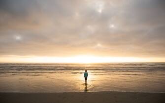 Boy walk out to waves and Pacific Ocean at sunset.