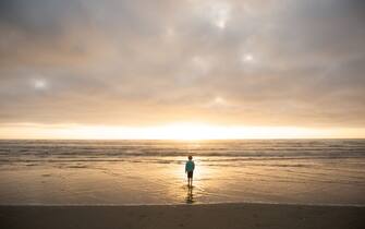 590946459 Boy walk out to waves and Pacific Ocean at sunset.