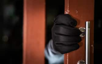 dangerous masked burglar with crowbar breaking into a victim's home door