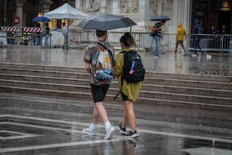 Persone si riparano con gli ombrelli dalla pioggia nel centro di Milano, 18 agosto 2022. ANSA/MATTEO CORNER