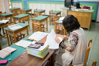 Female teacher is marking exam papers in classroom