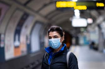 A middle-aged woman with dark hair using a health mask on the London Underground metro system during the Coronavirus outbreak