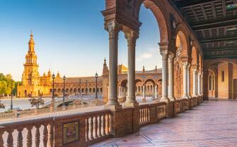Sunrise on the old tower seen from colonnade of the semi-circular portico, Plaza de Espana, Seville, Andalusia, Spain